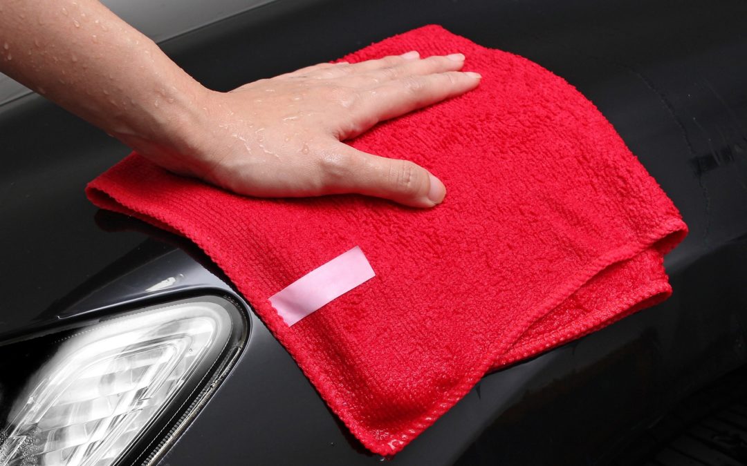 A Hand Wiping Down the Front of a Black Car with a Red Micro Fiber Cloth