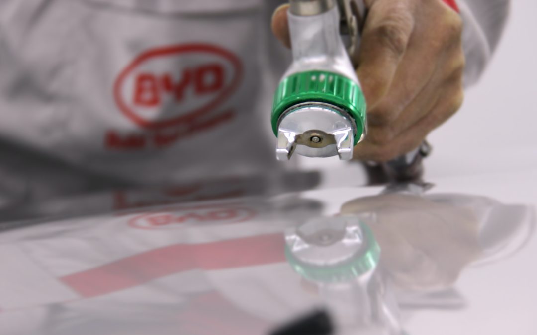 Close up of a man pointing a silver spray gun with a green tip at a white car hood