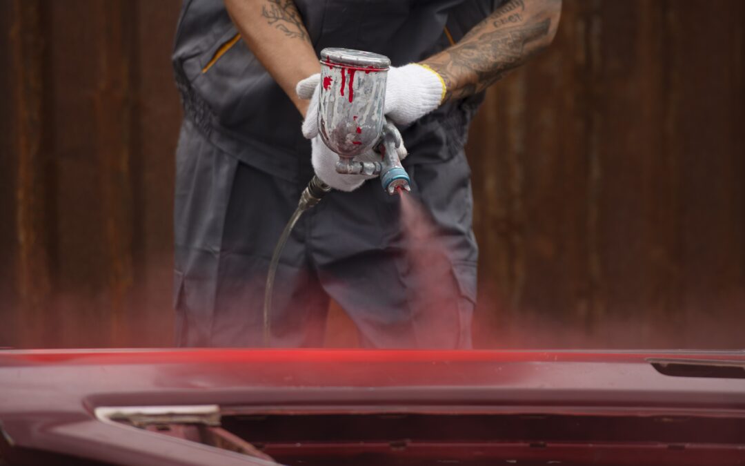 Tattooed Man with white gloves on Painting a car door with a Spray Gun