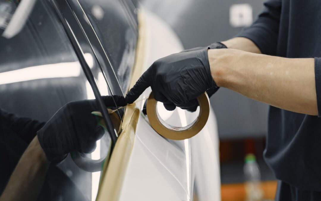 Man in Black Gloves putting Masking Tape onto a car, preparing a car for painting